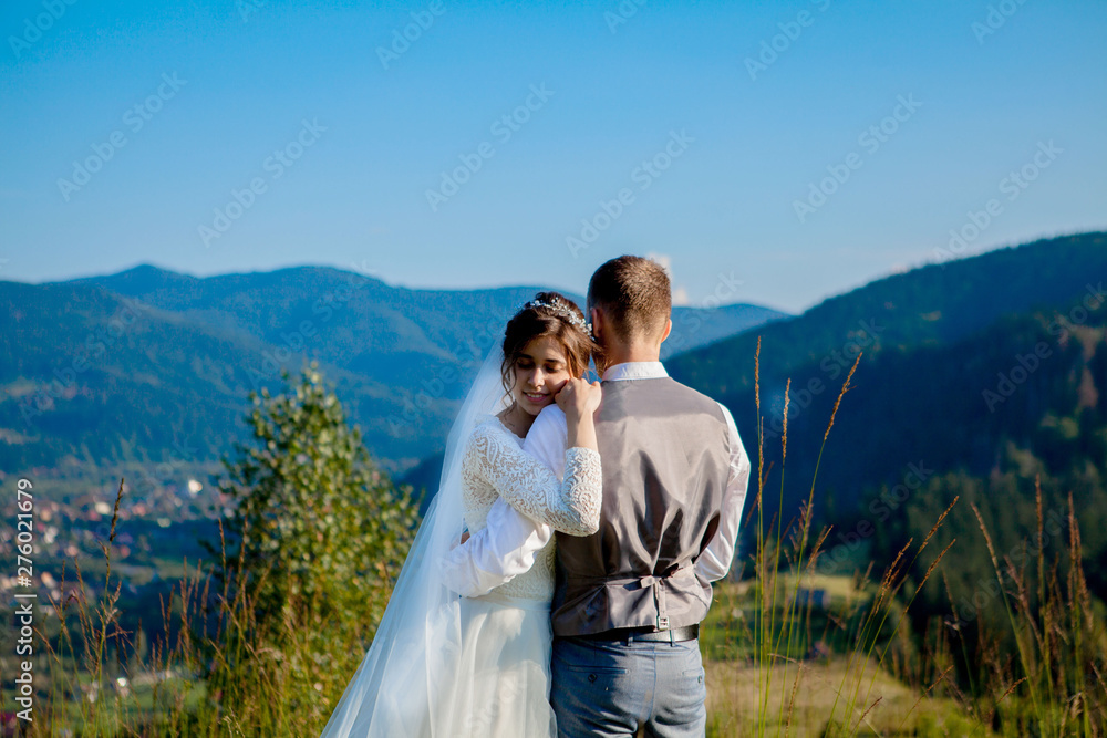 Newlyweds smile and hug each other among the meadow on top of the mountain. Wedding walk in the woods in the mountains, the gentle emotions of the couple, photo for Valentine's Day Newlyweds smile and hug each other among the meadow on top of the mountain. Wedding walk in the woods in the mountains, the gentle emotions of the couple, photo for Valentine's Day