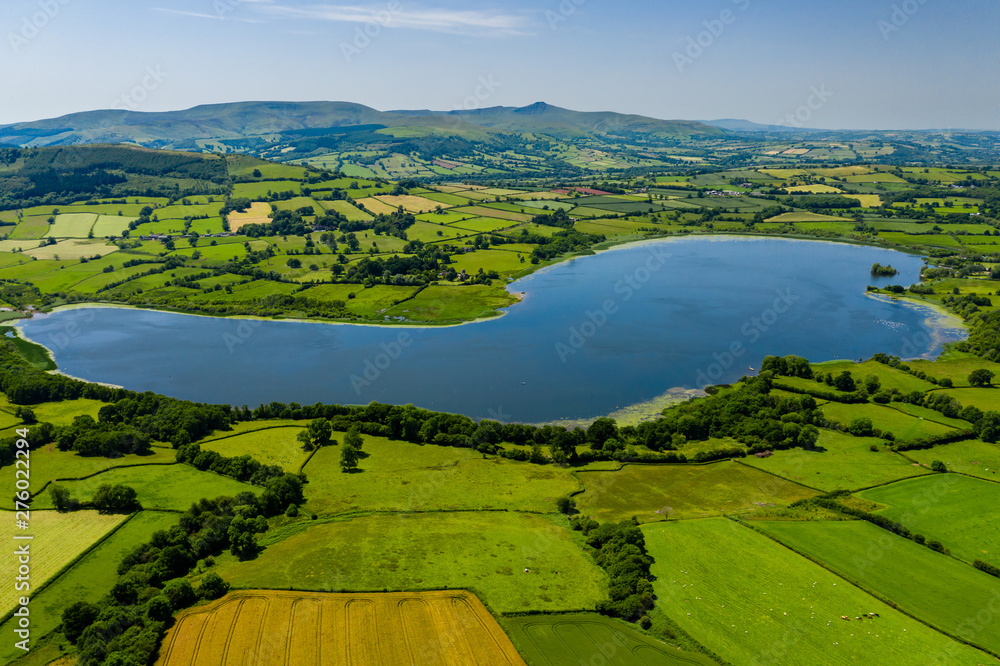 Aerial drone view of a lake surrounded by green farmland and fields in rural Wales (Llangorse Lake)