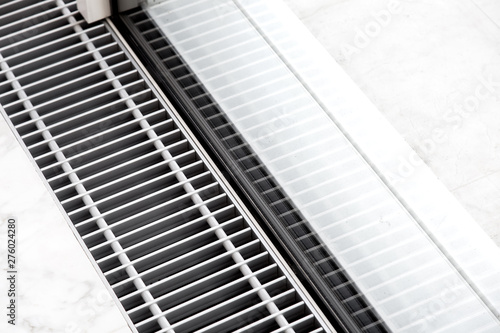 Heating grille with floor ventilation in white stone flooring near the panoramic window, close up of the air conditioning grille.