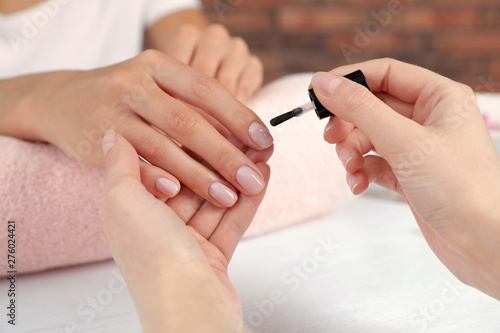 Manicurist applying polish on client s nails at table  closeup. Spa treatment
