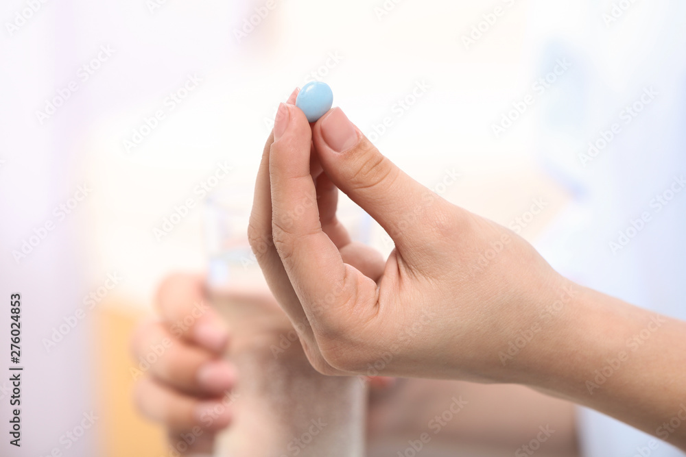 Obraz premium Woman holding pill and glass of water on blurred background, closeup. Space for text