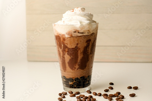 Ice coffee in the glass topped whipping cream with coffee beans. Cold summer drink on wooden background and copy space. Advertising for caramel mocha and chocolate beverage for the cafe. © paulynn