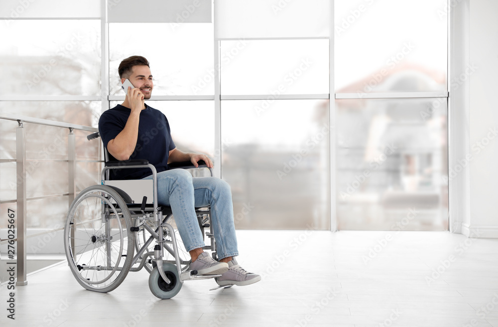 Young man in wheelchair talking on mobile phone near window indoors Young man in wheelchair talking on mobile phone near window indoors