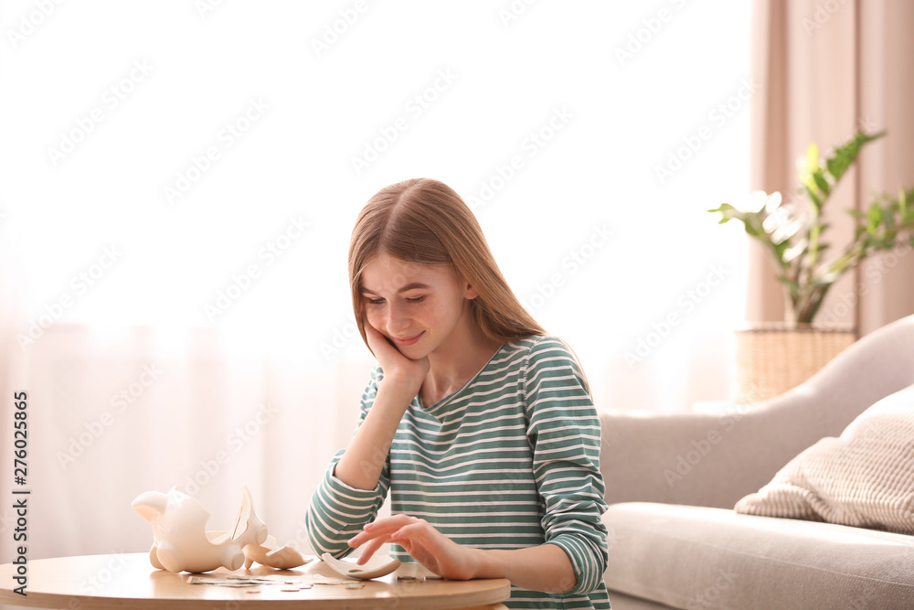 Φωτογραφία Teen girl with broken piggy bank and money at home