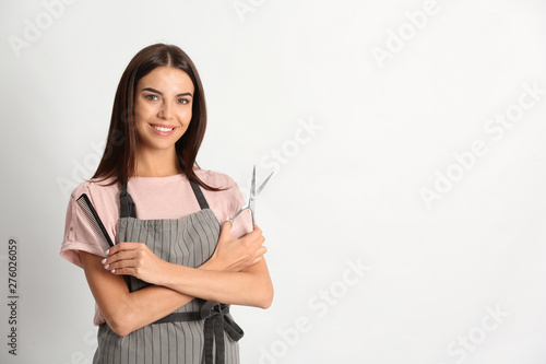 Quadro su tela Young hairstylist holding professional scissors and comb on light background