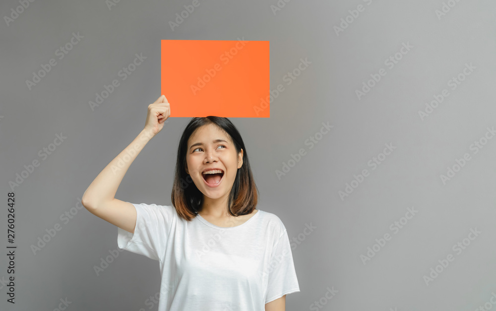 Asian woman of happy smiling holding a blank orange poster on gray background. with empty space for text. Asian woman of happy smiling holding a blank orange poster on gray background. with empty space for text.
