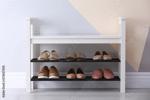 Shoe rack with different footwear near color wall, space for text. Stylish hallway interior