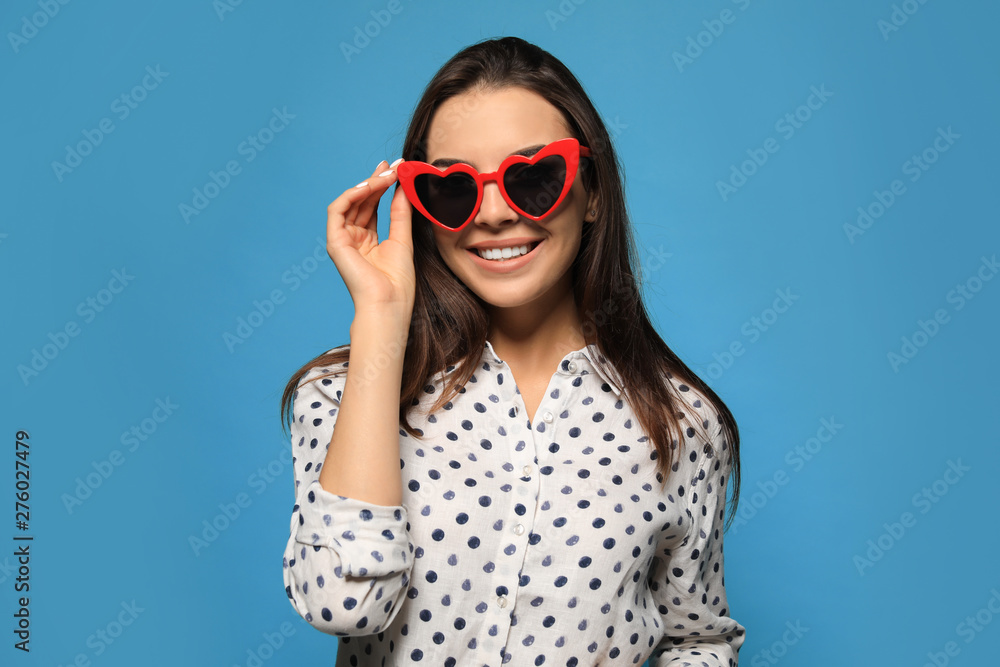 Fototapeta premium Portrait of beautiful young woman with heart shaped sunglasses on color background