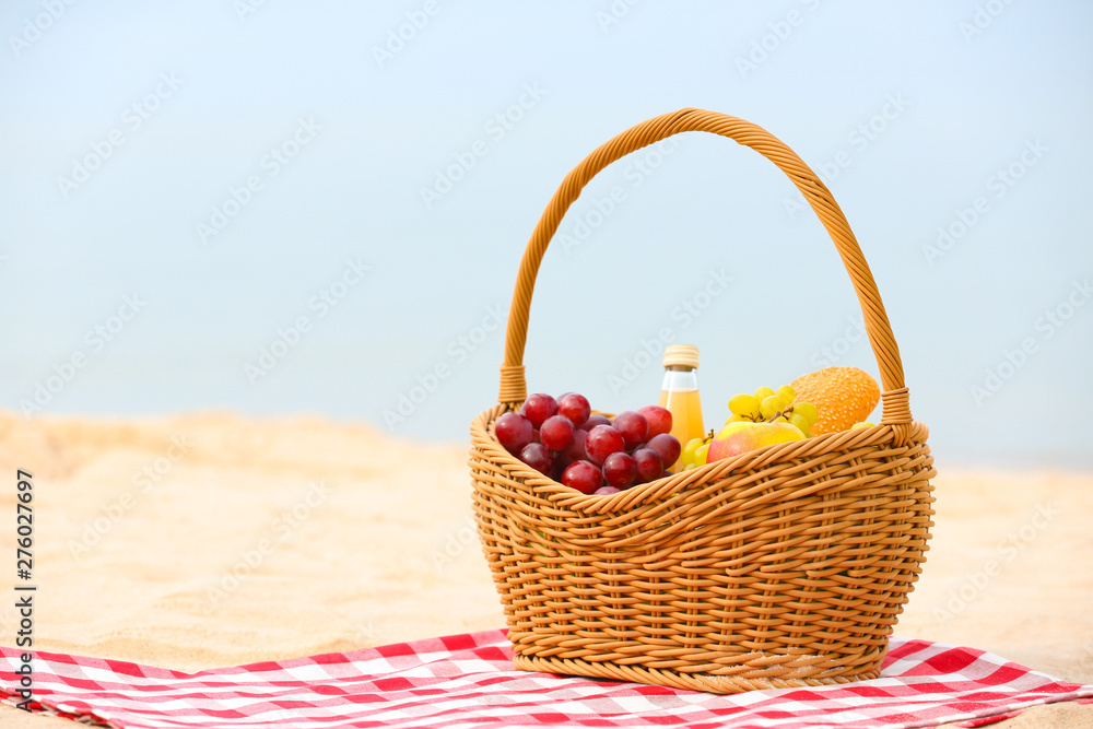 Wicker basket with food and juice on blanket near sea, space for text. Summer picnic Wicker basket with food and juice on blanket near sea, space for text. Summer picnic