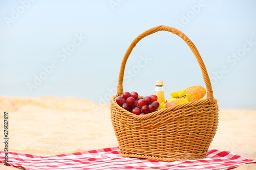 Wicker basket with food and juice on blanket near sea, space for text. Summer picnic