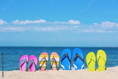 Composition with bright flip flops on sand near sea in summer. Beach accessories