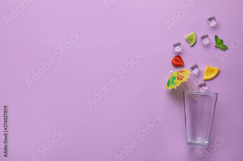 Flat lay composition with glass, ice and sliced fruits on color background, space for text. Summer cocktail recipe