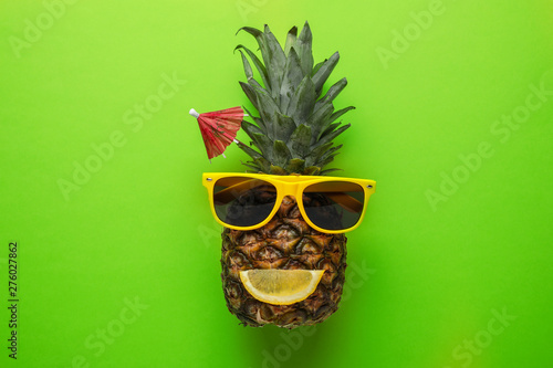 Funny face made of pineapple, sunglasses and citrus slice with cocktail umbrella on color background, top view