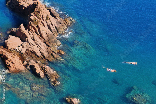 two divers swim in the blue sea lagoon with rocks in the mediterranean sea, aerial view