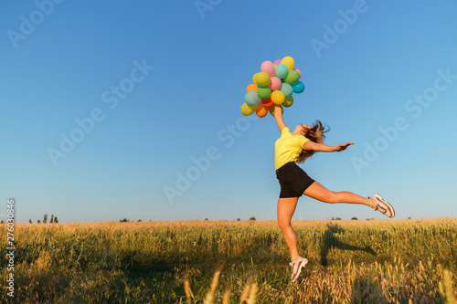 Happiness  dream  inspiration  motivation  summertime. Happy young carefree woman jumping with multicolored balloons at sunset