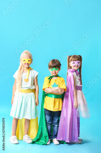 Cute little children dressed as superheroes on color background