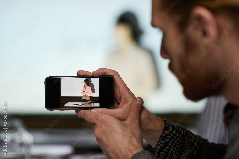 Fototapeta premium Close-up of man using smartphone while photographing Chinese speaker at conference, copy space