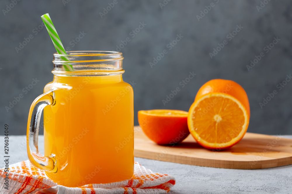 Freshly made citrus juice from oranges in a jar-mug with a straw on gray table Freshly made citrus juice from oranges in a jar-mug with a straw on gray table