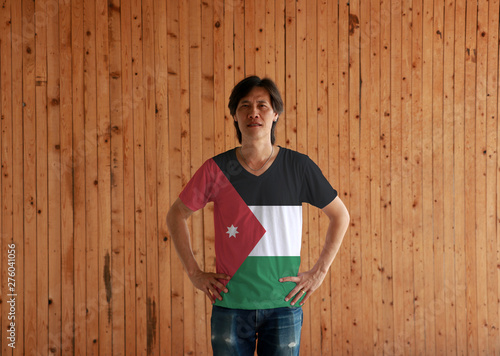 Man wearing Jordan flag color shirt and standing with akimbo on the wooden wall background.
