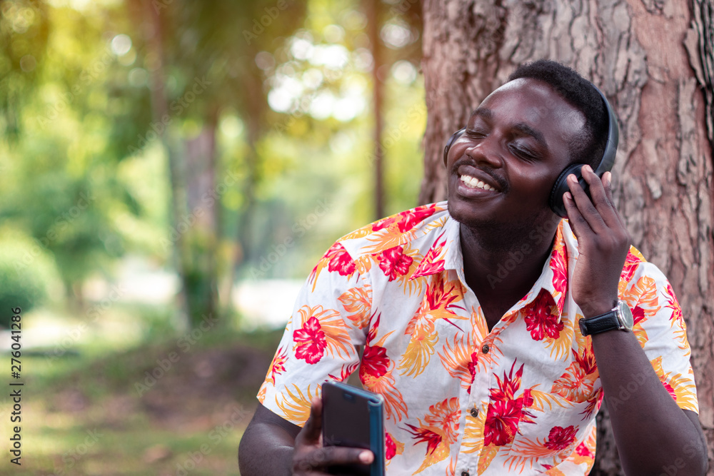 Obraz premium African man listening to music from smartphone with earphones against green natural background.