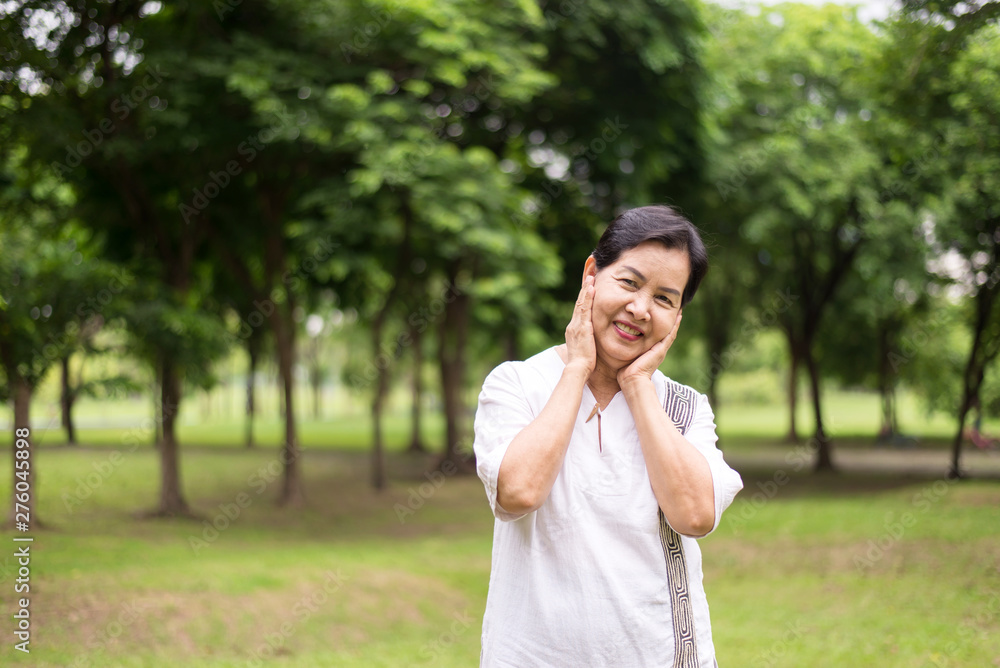 Portrait of elderly asian women standing and hand touching her cheek at park,Happy and smiling,Positive attitude thinking Portrait of elderly asian women standing and hand touching her cheek at park,Happy and smiling,Positive attitude thinking