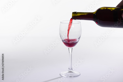 Red wine pouring into glass from bottle on white background with copy space