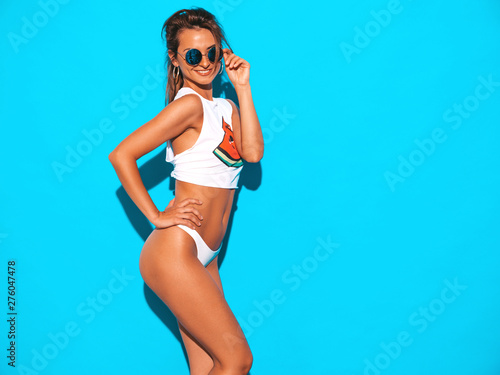Portrait of young beautiful sexy smiling hipster woman in white summer underpants and topic.Trendy girl in in sunglasses. Positive female going crazy.Funny model isolated on blue © halayalex