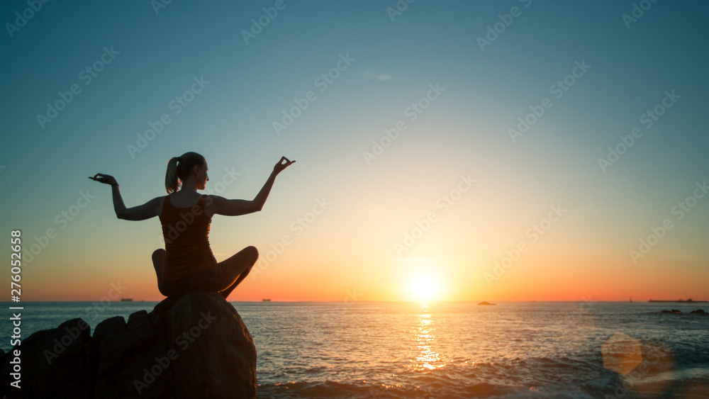 Silhouette young woman practicing concentration yoga during surreal sunset on the sea beach.