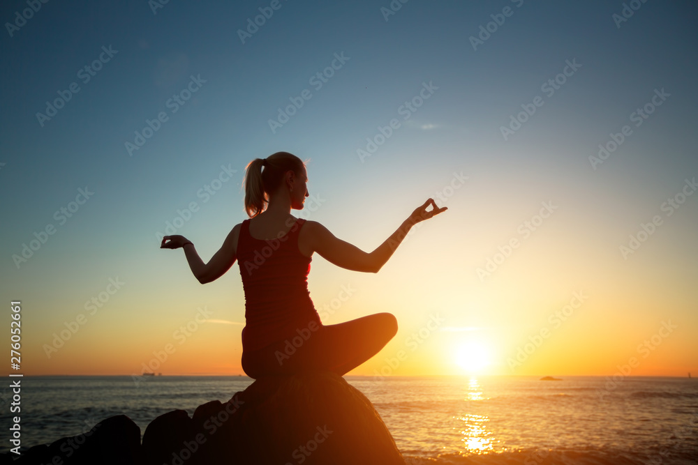 Silhouette young woman practicing yoga on the amazing sunset sea beach. Tranquility and concentration..