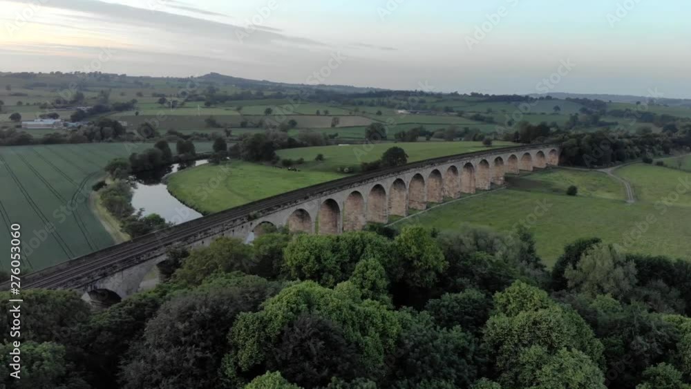 Cinematic aerial drone shot of train viaduct bridge crossing gentle flowing river in yorkshire countryside in england during golden hour sunset in summer Cinematic aerial drone shot of train viaduct bridge crossing gentle flowing river in yorkshire countryside in england during golden hour sunset in summer