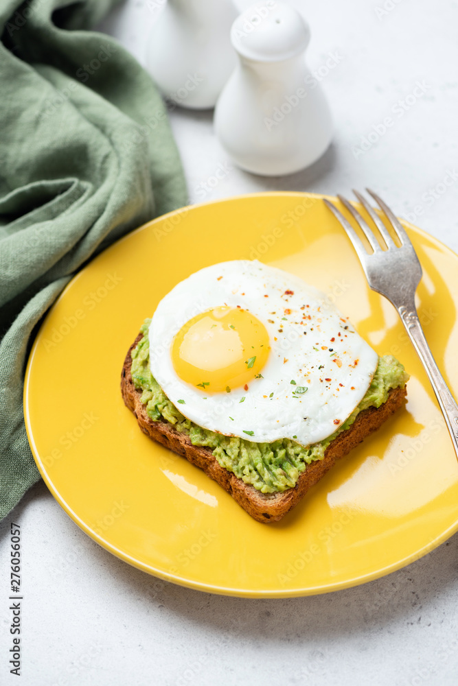 Toast with fried egg and avocado on yellow plate. Tasty breakfast, lunch or snack Toast with fried egg and avocado on yellow plate. Tasty breakfast, lunch or snack