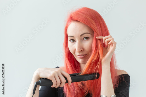 Hair Stylist, hairdresser and people concept - young woman with colored hair holding curling iron over white background