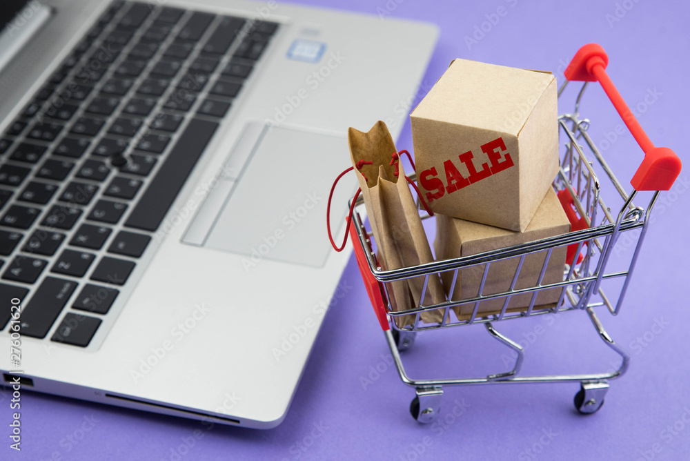 Shopping cart with purchases for sale - packages and boxes on the modern laptop. Online shopping and sale concept.