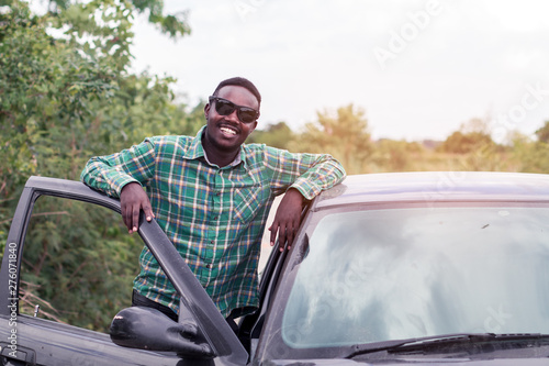 African man standing on the road near opened door of his car.