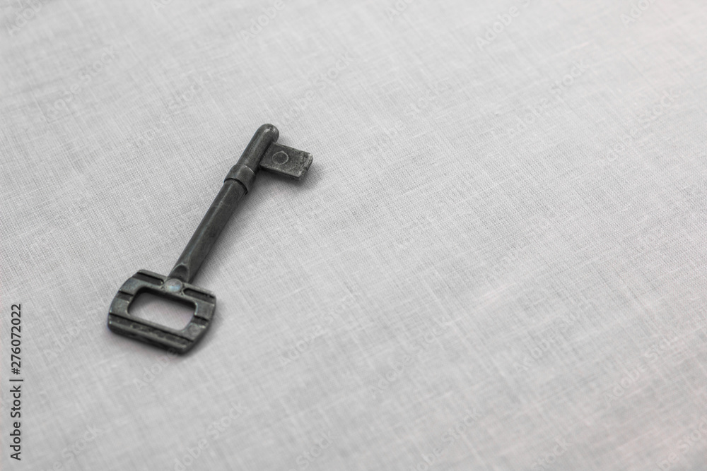 simple old iron key on a white textured table cloth perspective surface background wallpaper pattern empty space for copy or text simple old iron key on a white textured table cloth perspective surface background wallpaper pattern empty space for copy or text