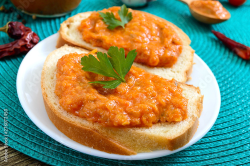 Delicious squash caviar in a jar and spread on slices of white bread on the table. Homemade caviar with zucchini, garlic, carrots, tomato sauce. Vegan cuisine. Close up