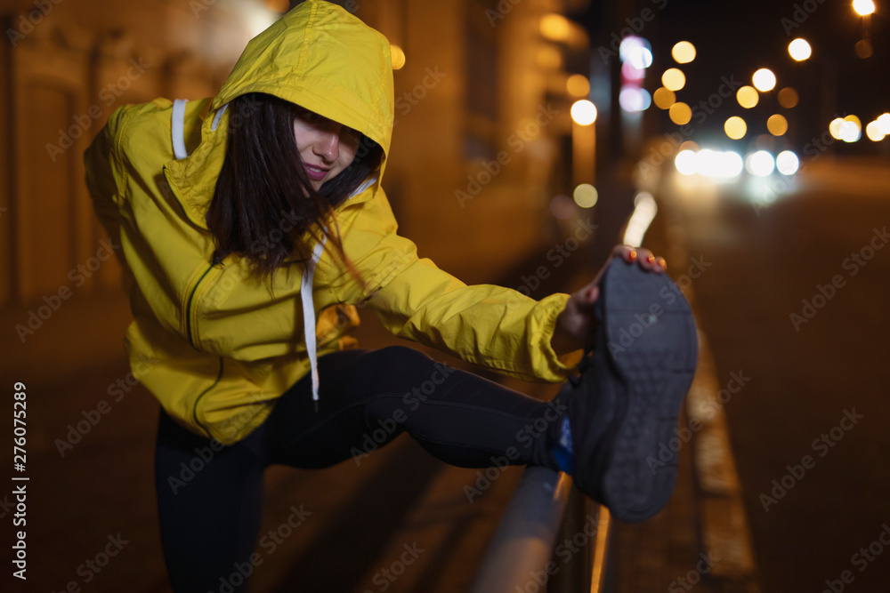 Sport woman stretches her leg at the night city, late training