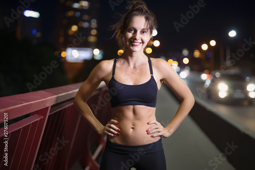 Smiling sport woman portrait on the night bridge, pretty female athlete