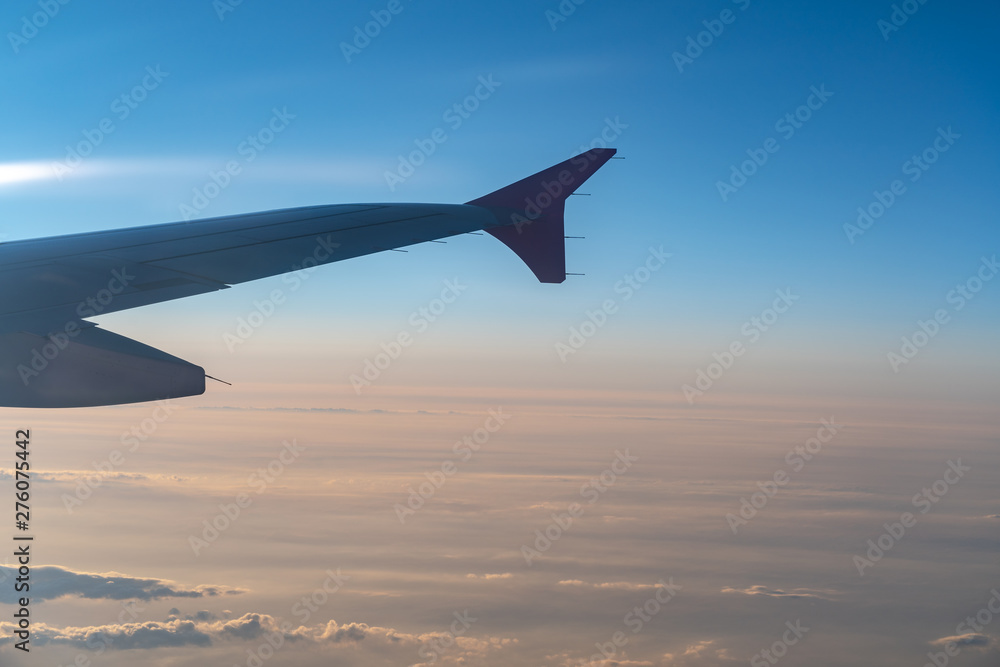 Up in the air, view of aircraft wing silhouette with dark blue sky horizon and cloud background in sunset time, viewed from airplane window