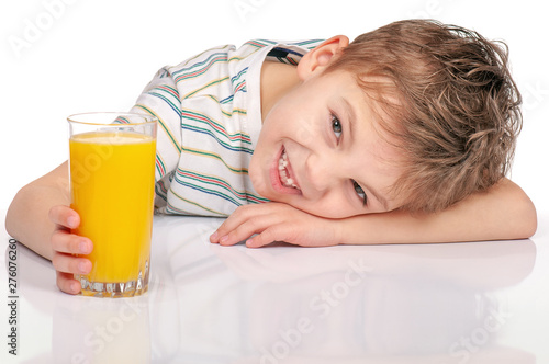 Portrait of happy little boy with glass of orange juice sitting at table on white background.