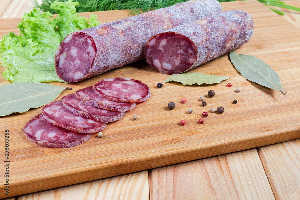 Partly sliced dry-cured sausage, greens, spices on cutting board Partly sliced dry-cured sausage, greens, spices on cutting board