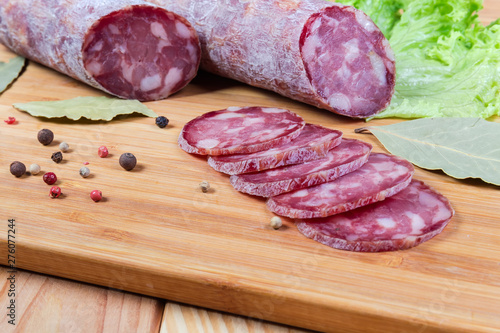 Partly sliced dry-cured sausage, greens, spices close-up