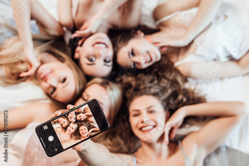 Portrait of sexy, cheerful girls in night wear lying on bed, making selfie, looking and posing at camera..
