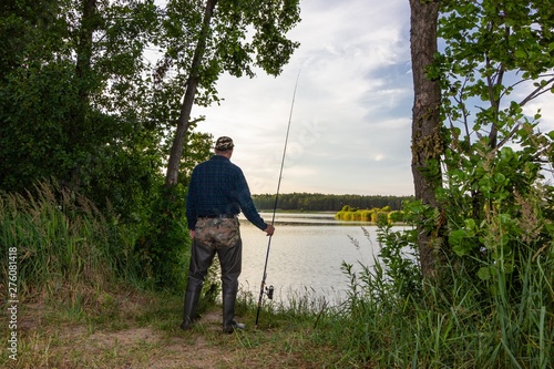 Angler standing on the shore of the lake during summer day