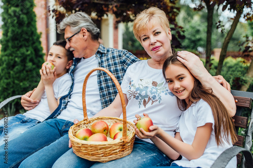 Grandparents sitting outdoors with their grandchildren and smiling with basket apples. Lovely concept.