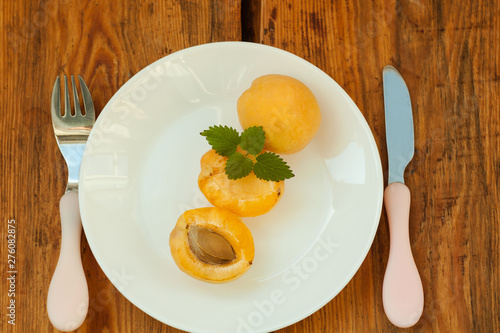 Ripe fresh apricot fruits on a white plate on the wooden background. Copy space, delisious healthy food.