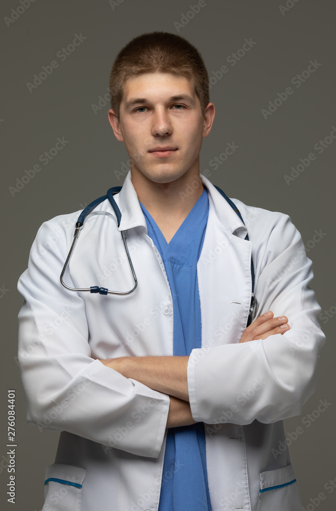 Closeup shot of young caucasian man doctor standing with crossed arms in white uniform against grey background looking perfectly confident. Closeup shot of young caucasian man doctor standing with crossed arms in white uniform against grey background looking perfectly confident.