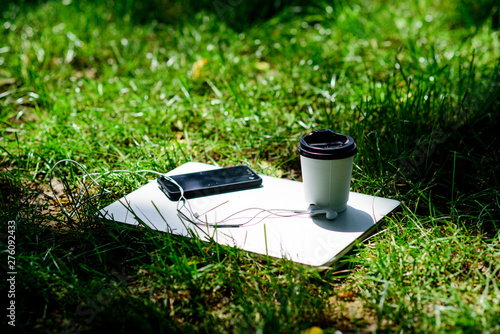 university students life. Online shopping. agile business. Online study. notebook with headset of mobile phone and coffee to go on green grass. working place outdoor. Free music. summer vibes. Relax photo