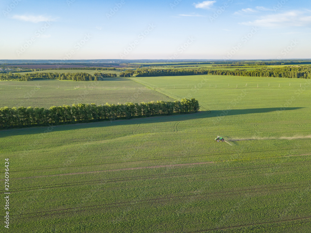 Aerial view of a farm tractor in a green field during spraying and irrigation with pesticides and toxins for growing food, vegetables and fruits. Agriculture industry.