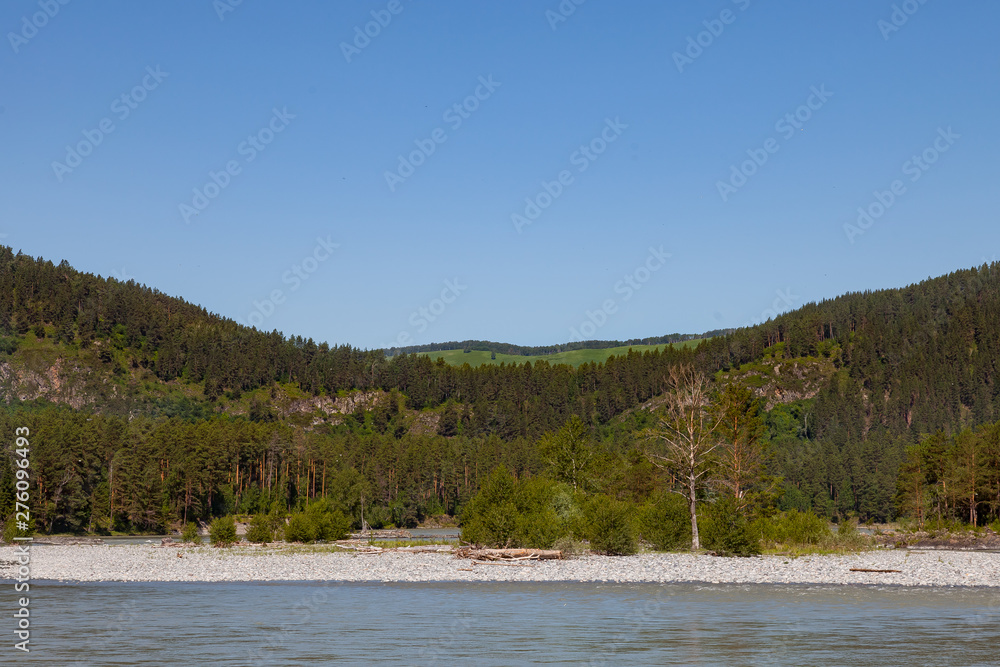 summer landscape on the river with stones and two mountains covered with green coniferous trees. travel and outdoor recreation.